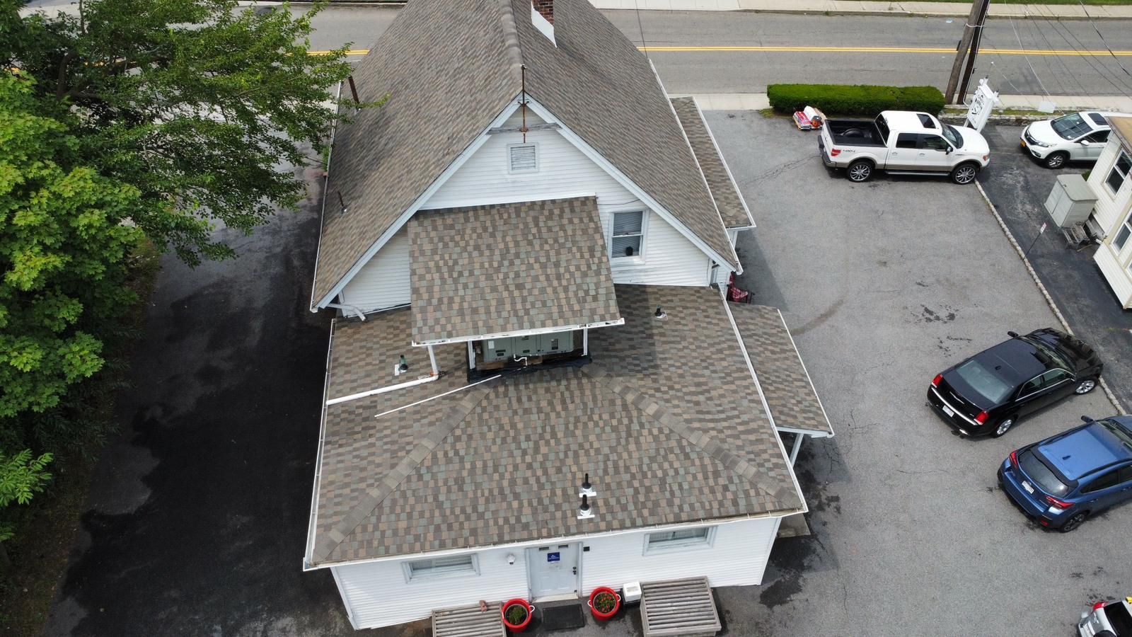 Overhead view of a white building with brown roof. Cars are parked in a paved lot beside it.