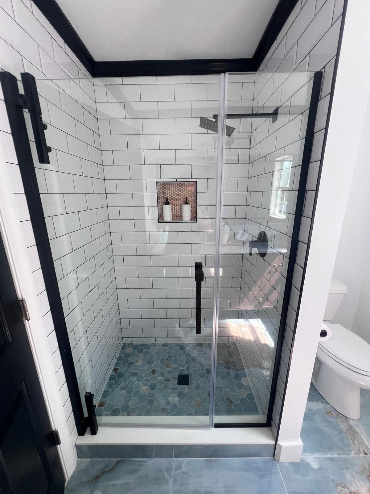 Modern shower with black trim, glass door, white brick tile walls, and blue mosaic floor.