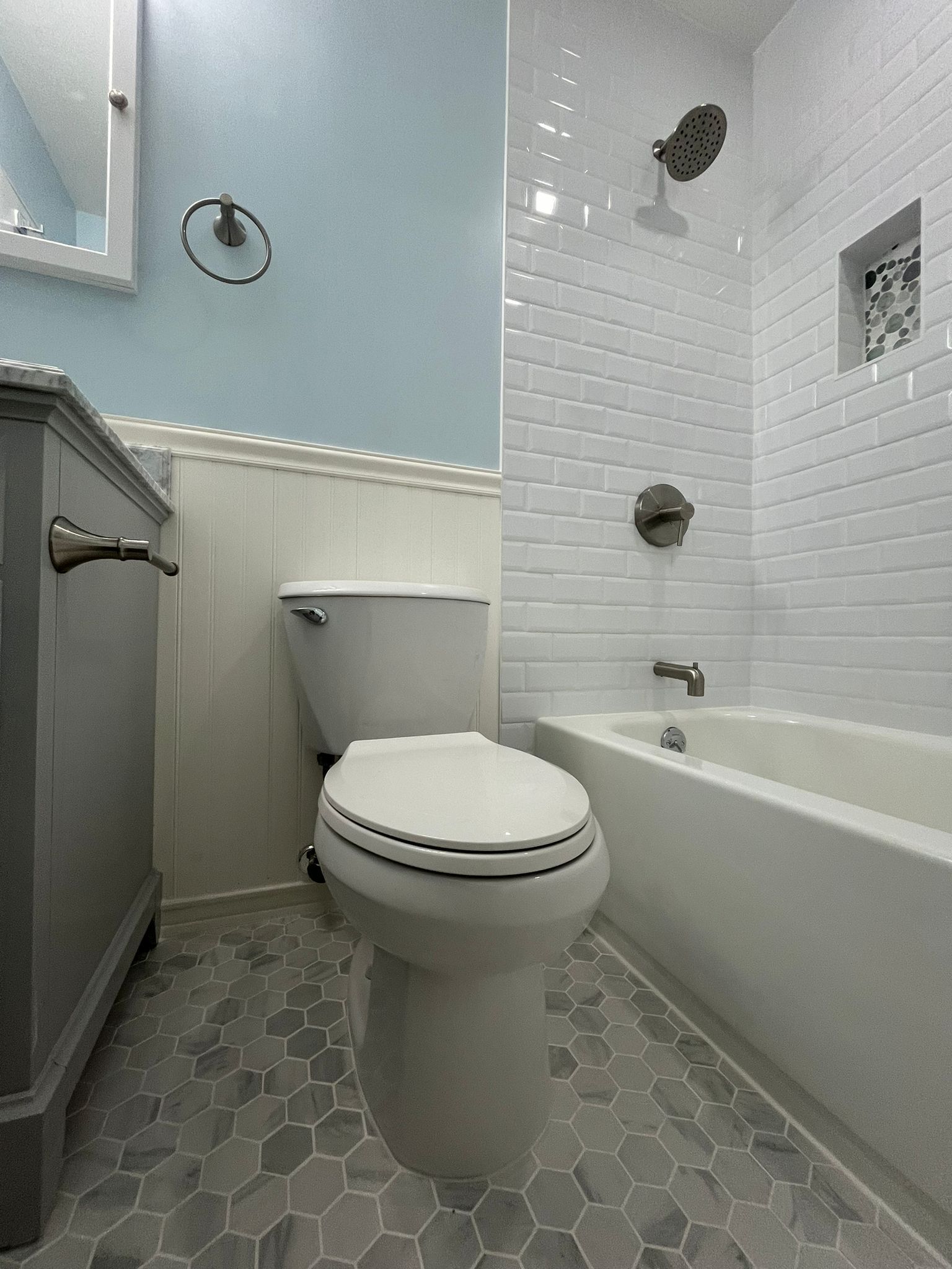 Bathroom with white tiling, blue walls, a toilet, tub and gray hexagon floor tiles.