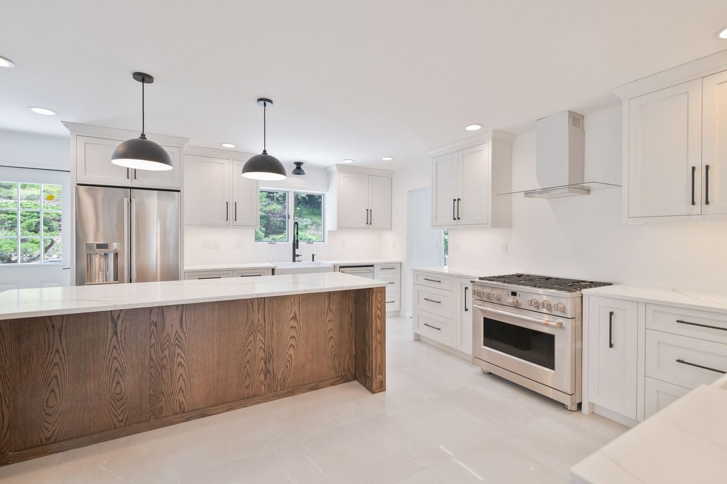 Bright white kitchen with a brown island, stainless steel appliances, and pendant lights.