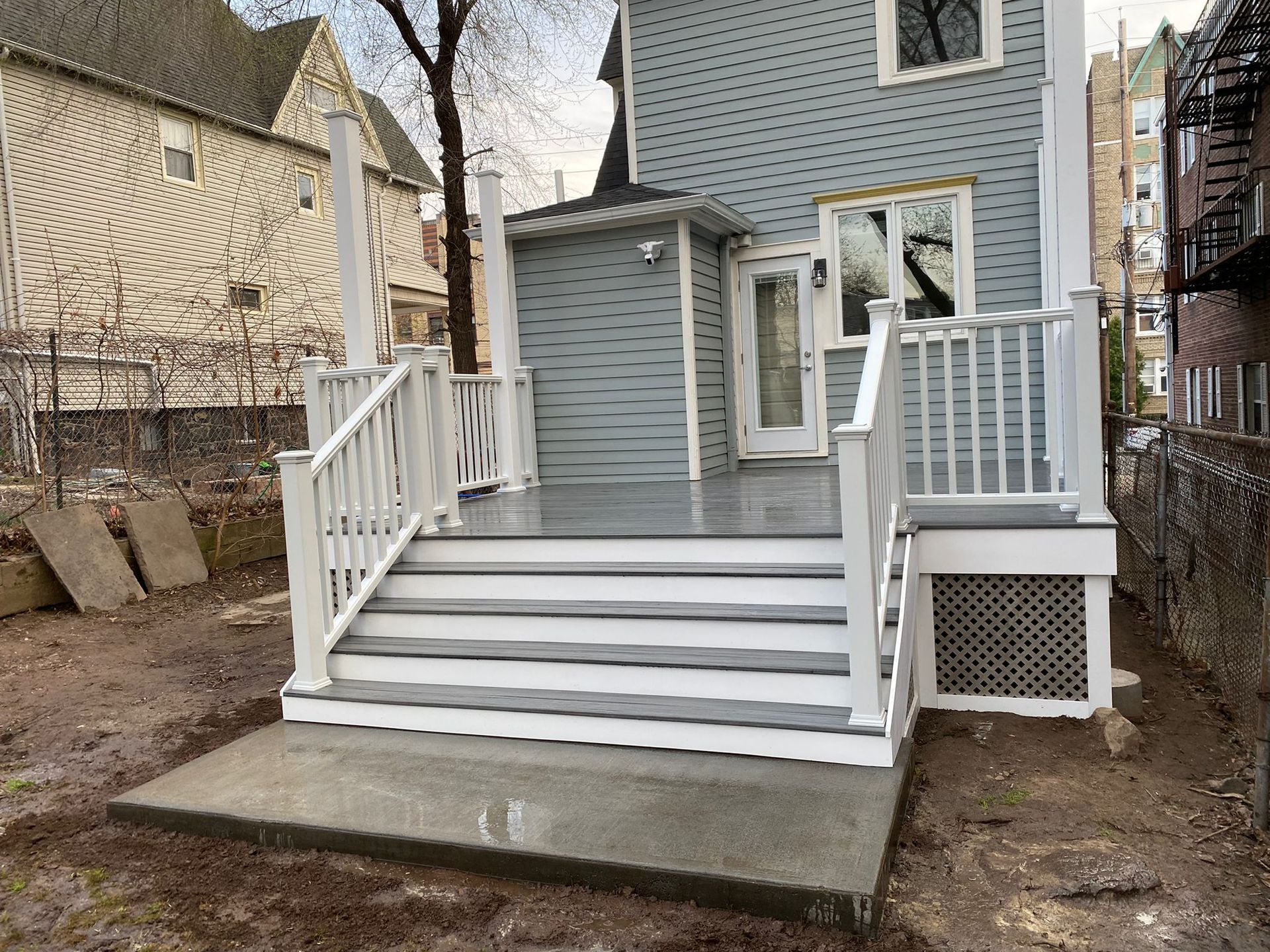 New deck with stairs, white railings, grey steps, and a door leading to a blue house.