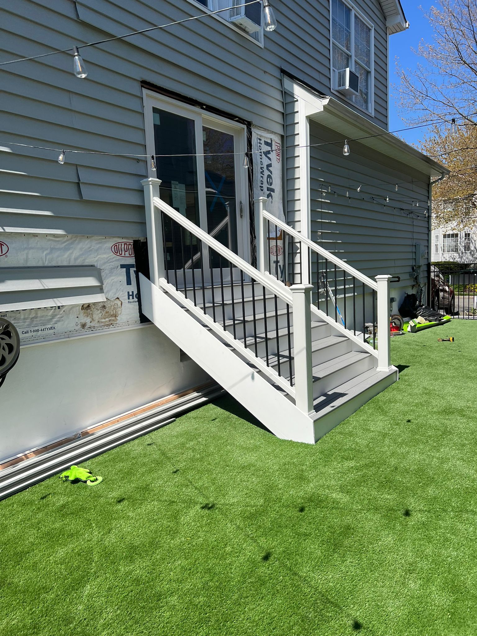 Exterior view of gray house with white and black deck stairs leading to a door, green lawn.