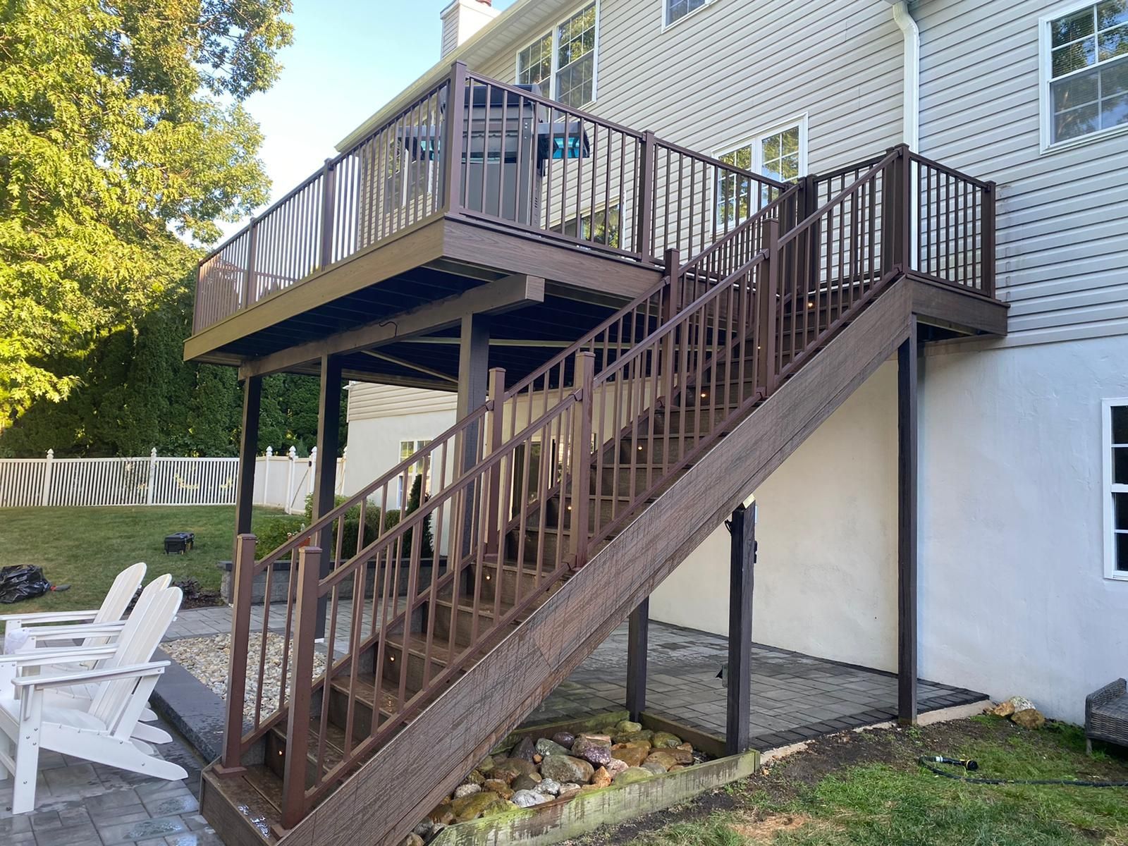 Brown wooden deck with stairs leading to a two-level deck on the back of a house.