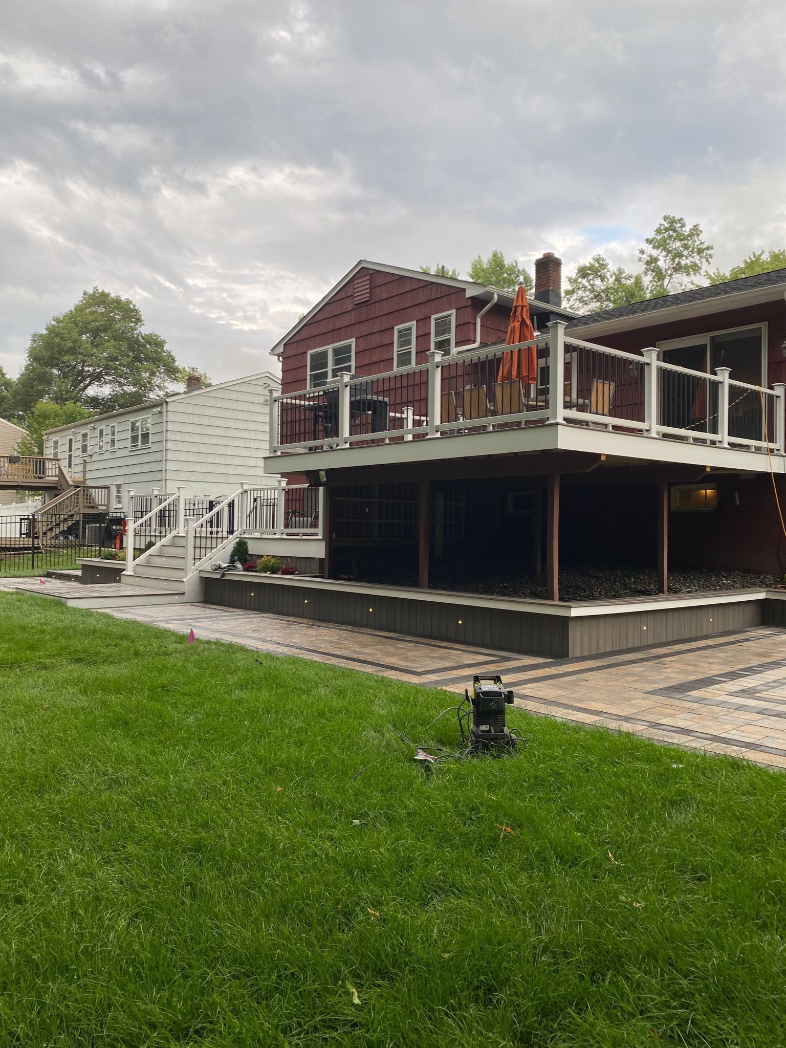 A red house with a large deck overlooking a lawn and patio under an overcast sky.