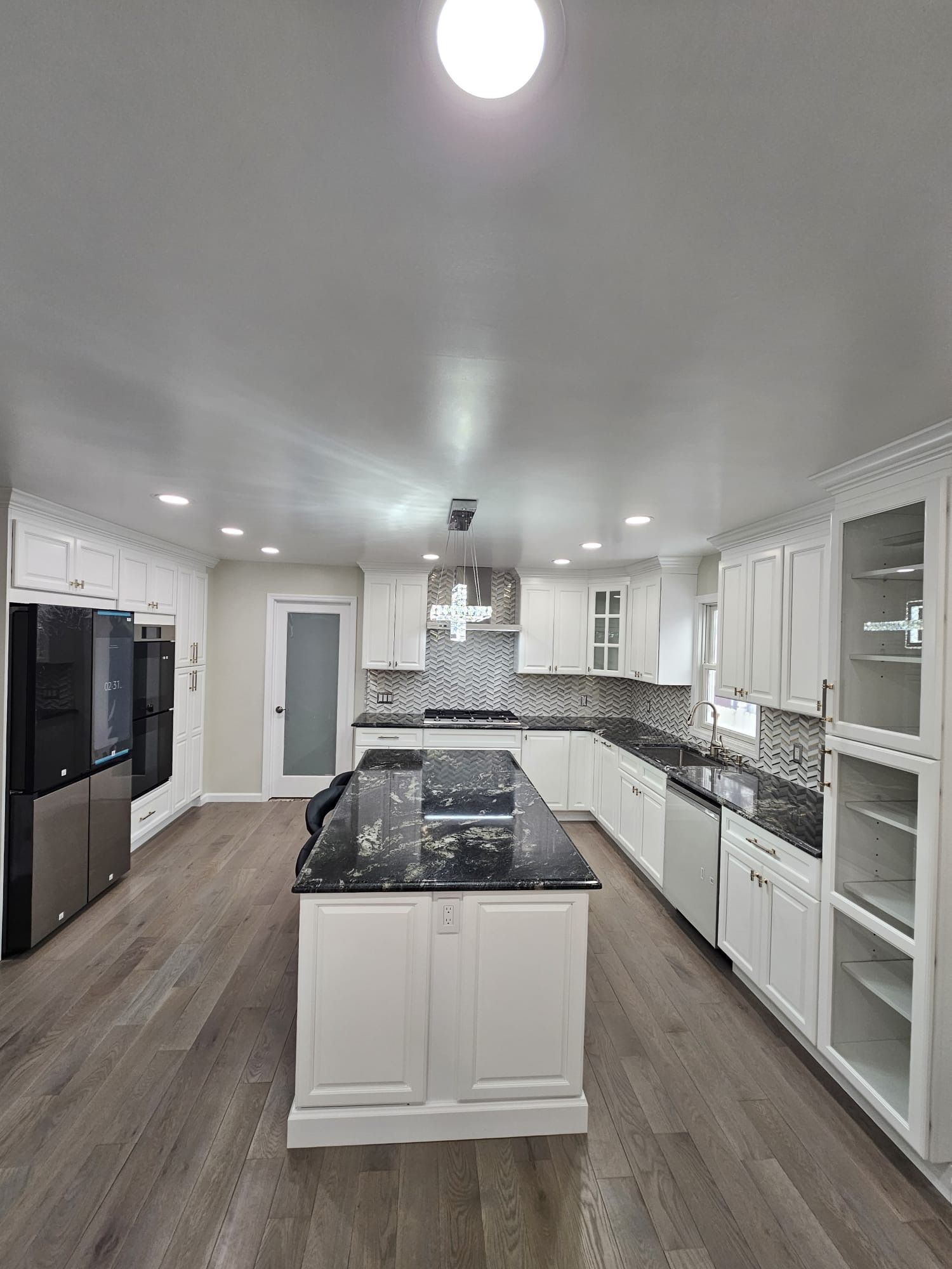 White kitchen with black granite countertops, island, stainless steel appliances, and wood floors.