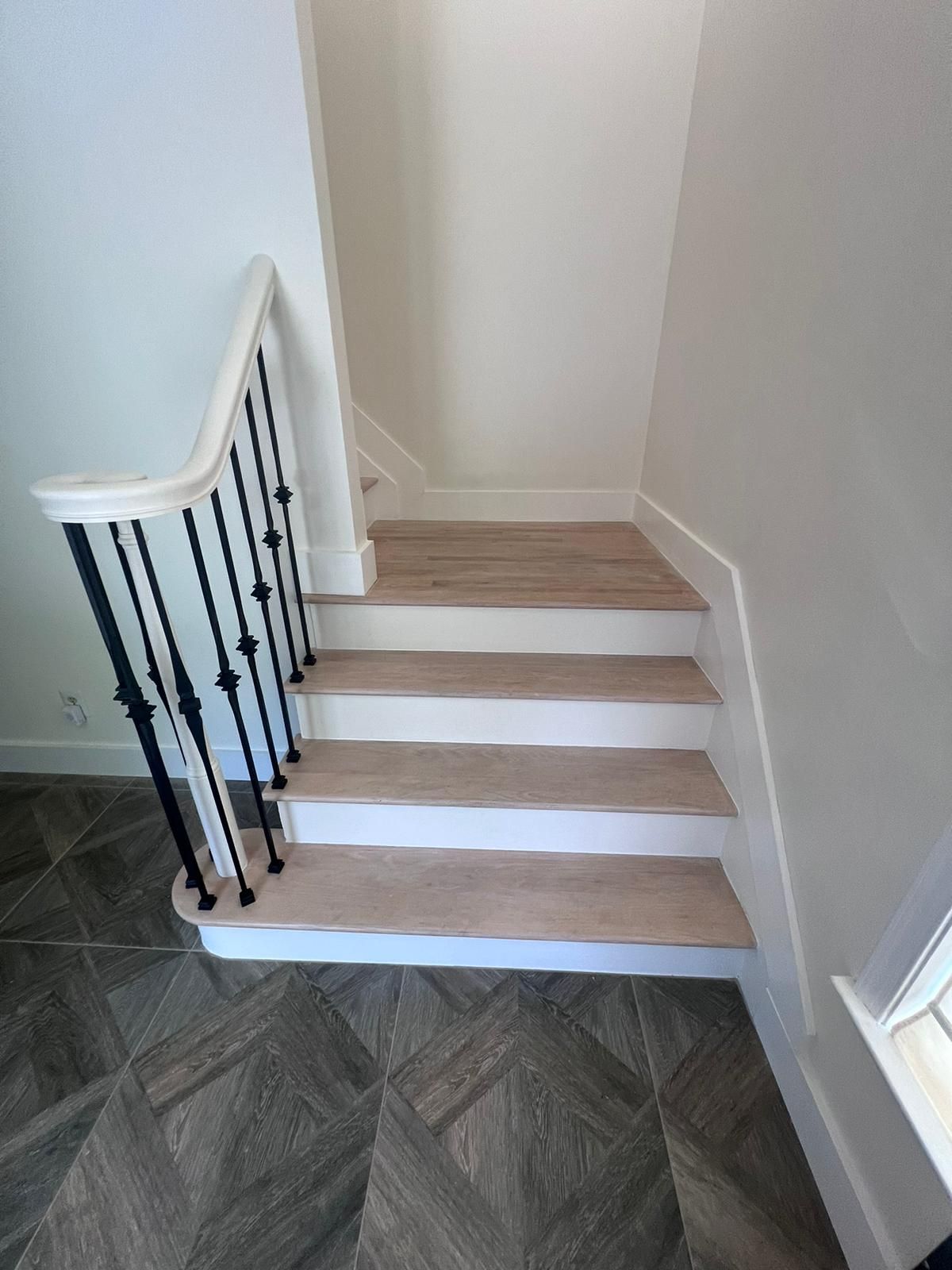 Staircase with light wood steps, white risers, and black iron balusters.