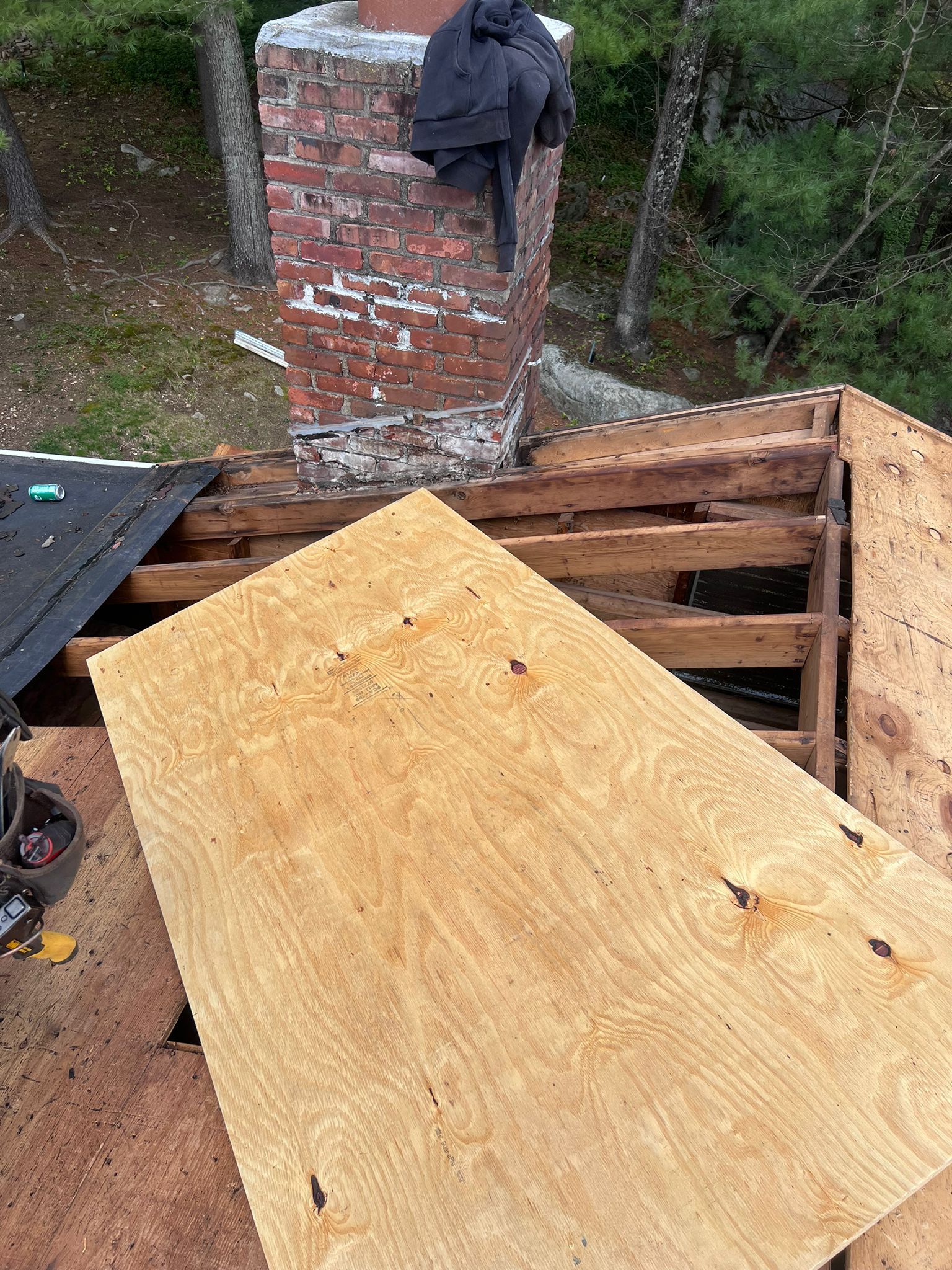 Roof repair scene: Plywood board on damaged wooden rafters near a brick chimney.
