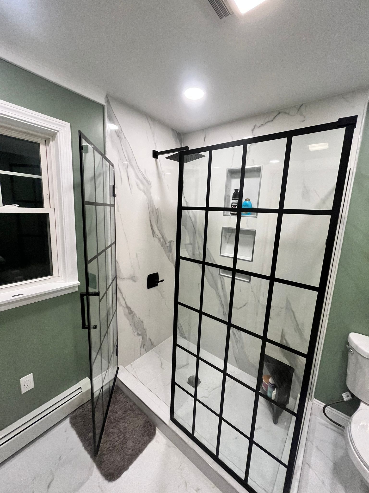 Modern shower with black grid frame, marble-look tile, and green wall. A small dog is visible inside.