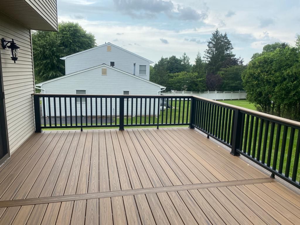 Wooden deck with black railing, overlooking a backyard with trees and houses, cloudy sky.