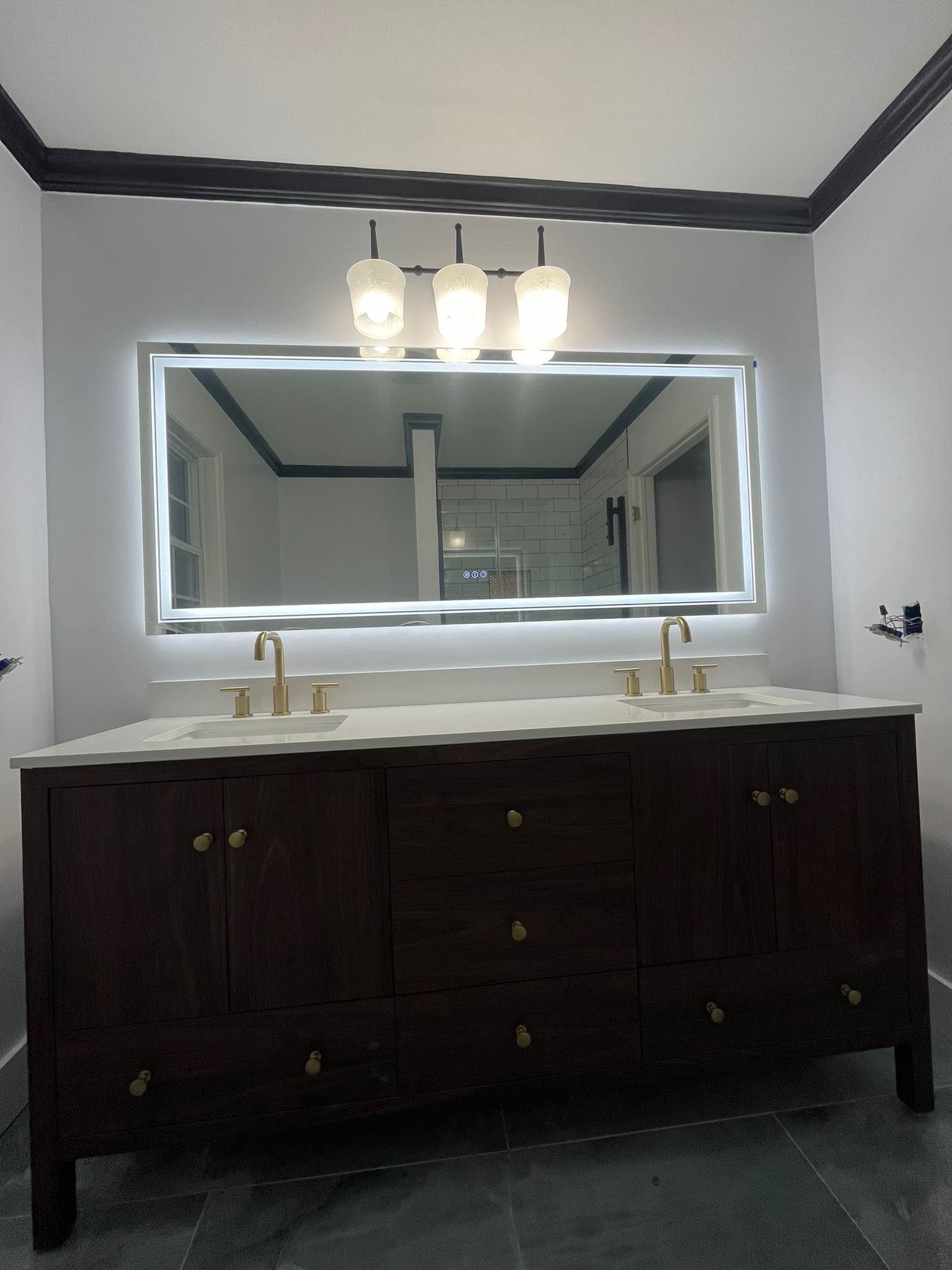Dark wood vanity with a white countertop, gold fixtures, and a lighted mirror in a bathroom.