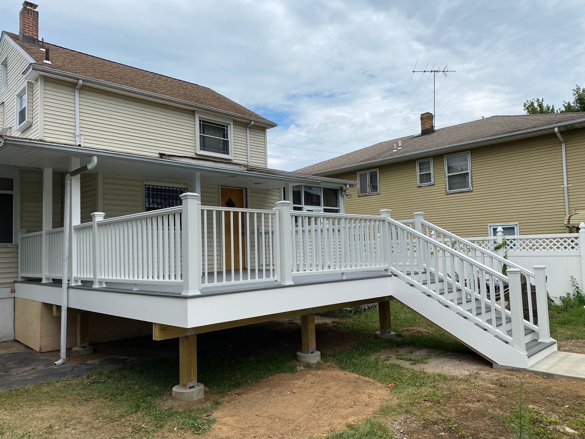White deck with railings and steps attached to a two-story house.