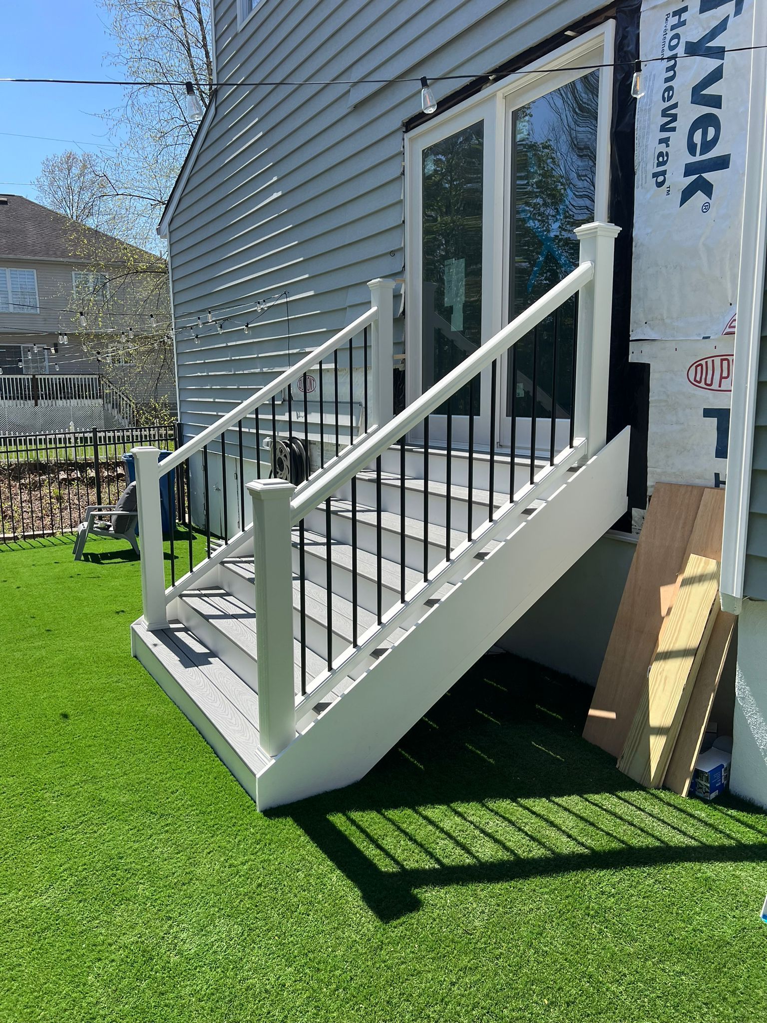 Outdoor staircase with white railing, black spindles, and grey steps leading to a glass door, on green lawn.