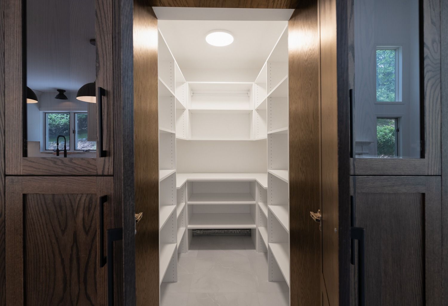 Walk-in pantry with white shelves, recessed lighting, and wooden frame. Doors are partially visible.
