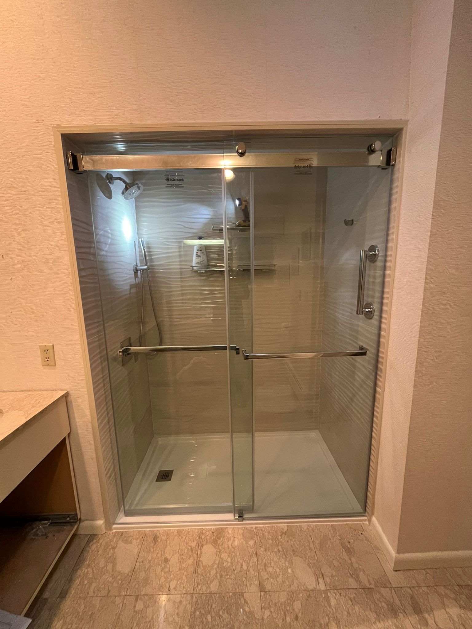 Shower with glass doors and chrome hardware in a bathroom with textured walls.