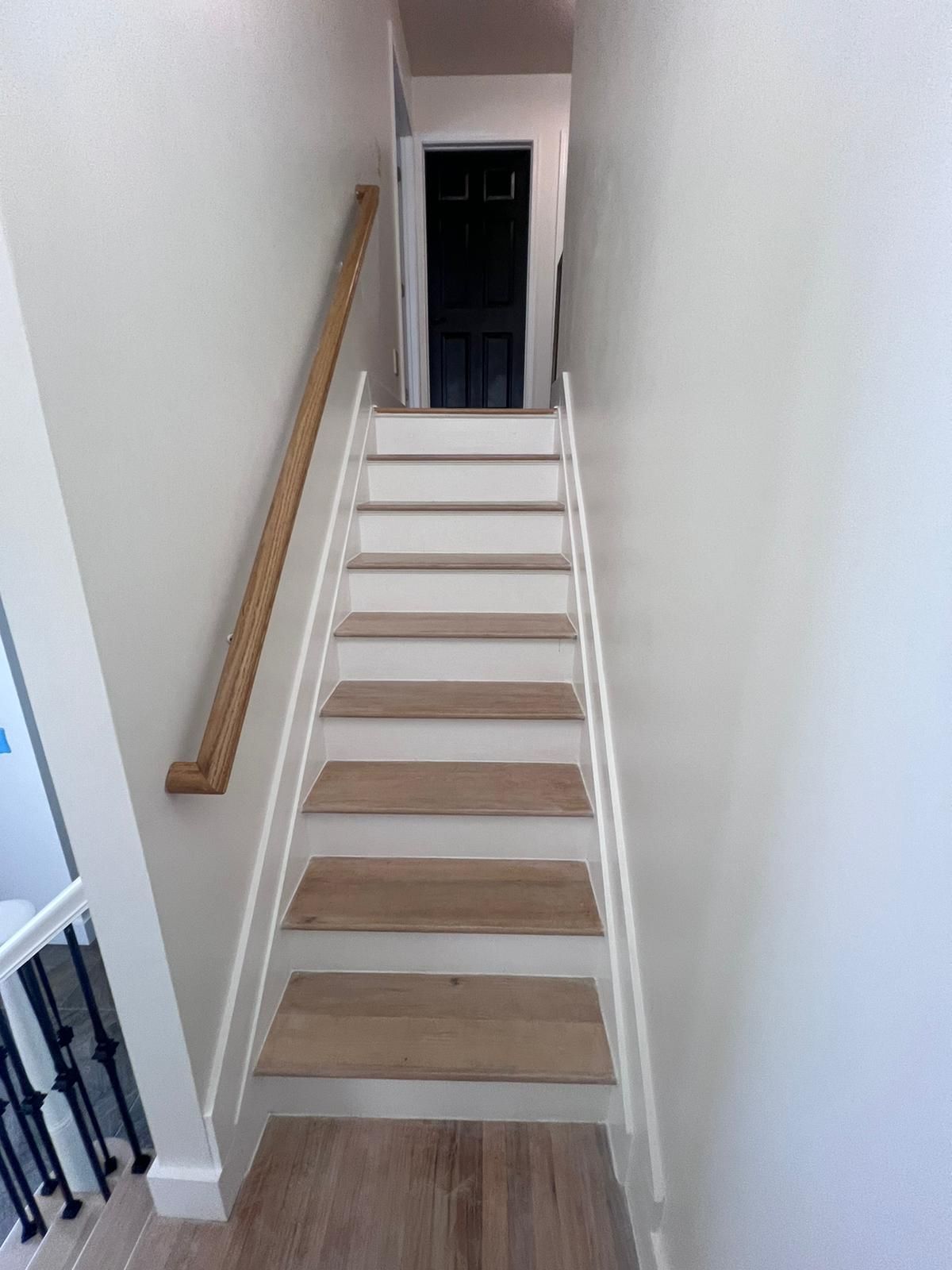 Staircase with light wood treads, white risers, and a wooden handrail, leading up to a dark doorway.