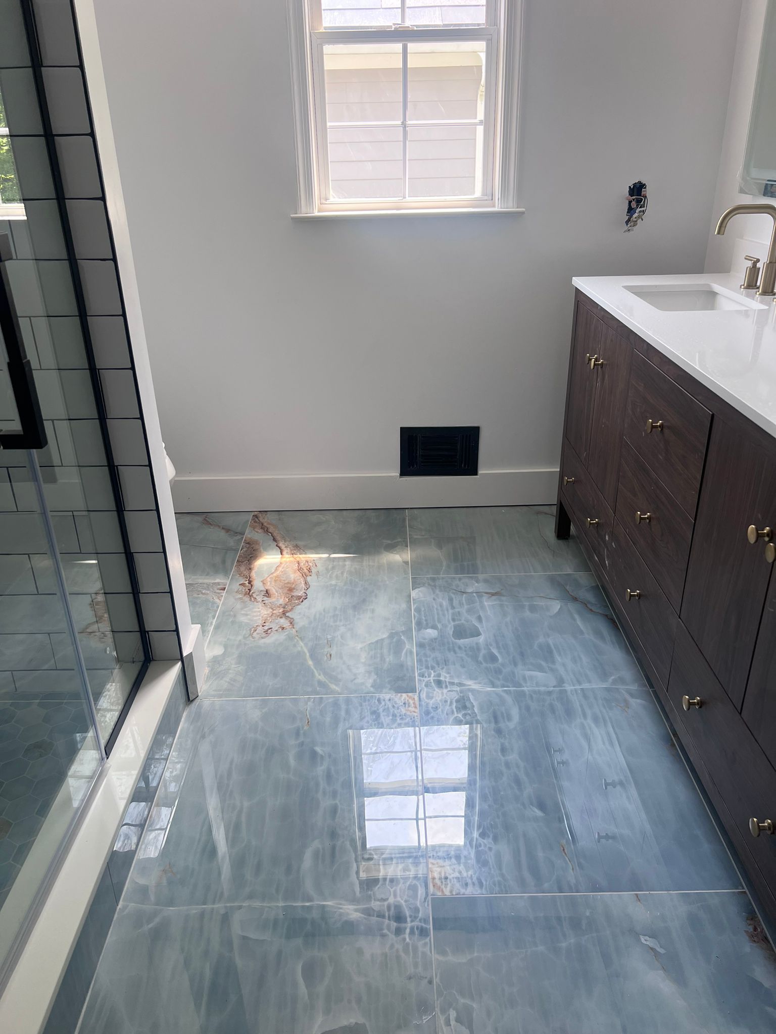 Bathroom with blue-gray tile floor, dark wood vanity, white walls, small window, and shower with glass door.