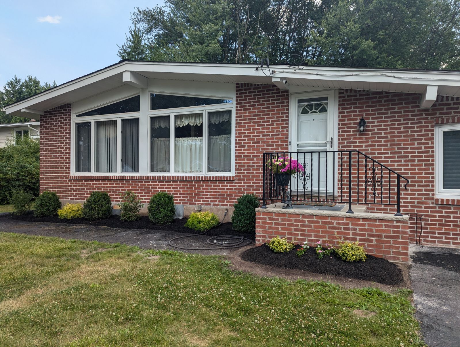 Red brick house with white trim, a small porch, and green landscaping.