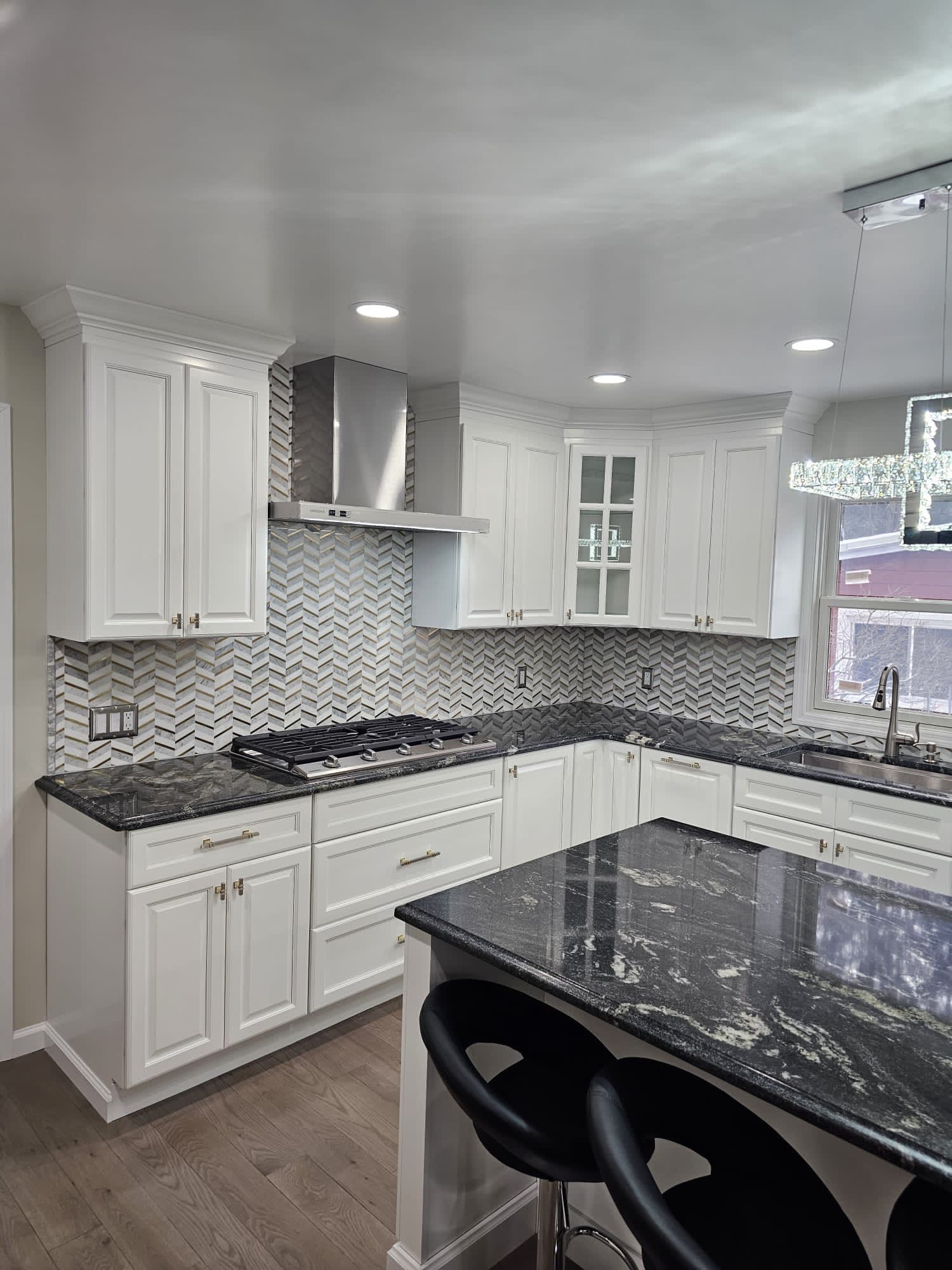 White kitchen with black countertops, stainless steel range hood, and breakfast bar with stools.