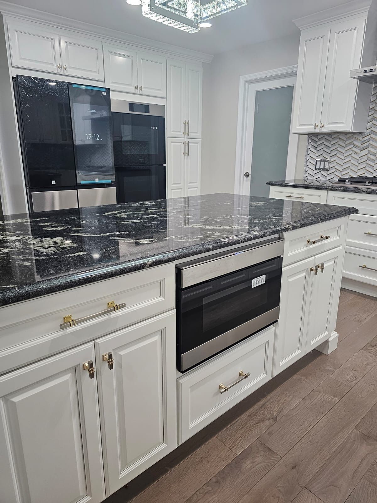 White kitchen with a black granite island. Stainless steel appliances and light wood floors.