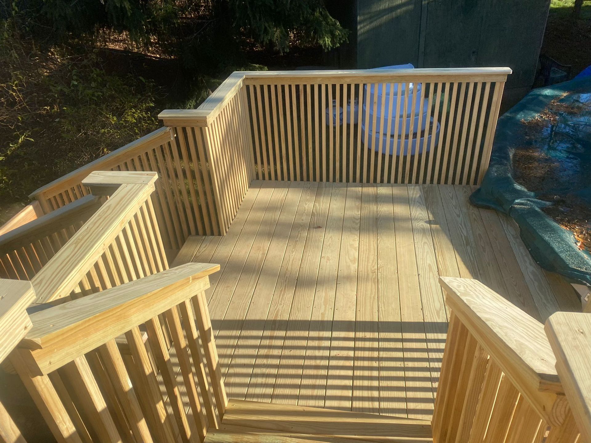 Wooden deck with stairs, vertical railing, and sunlight casting shadows.