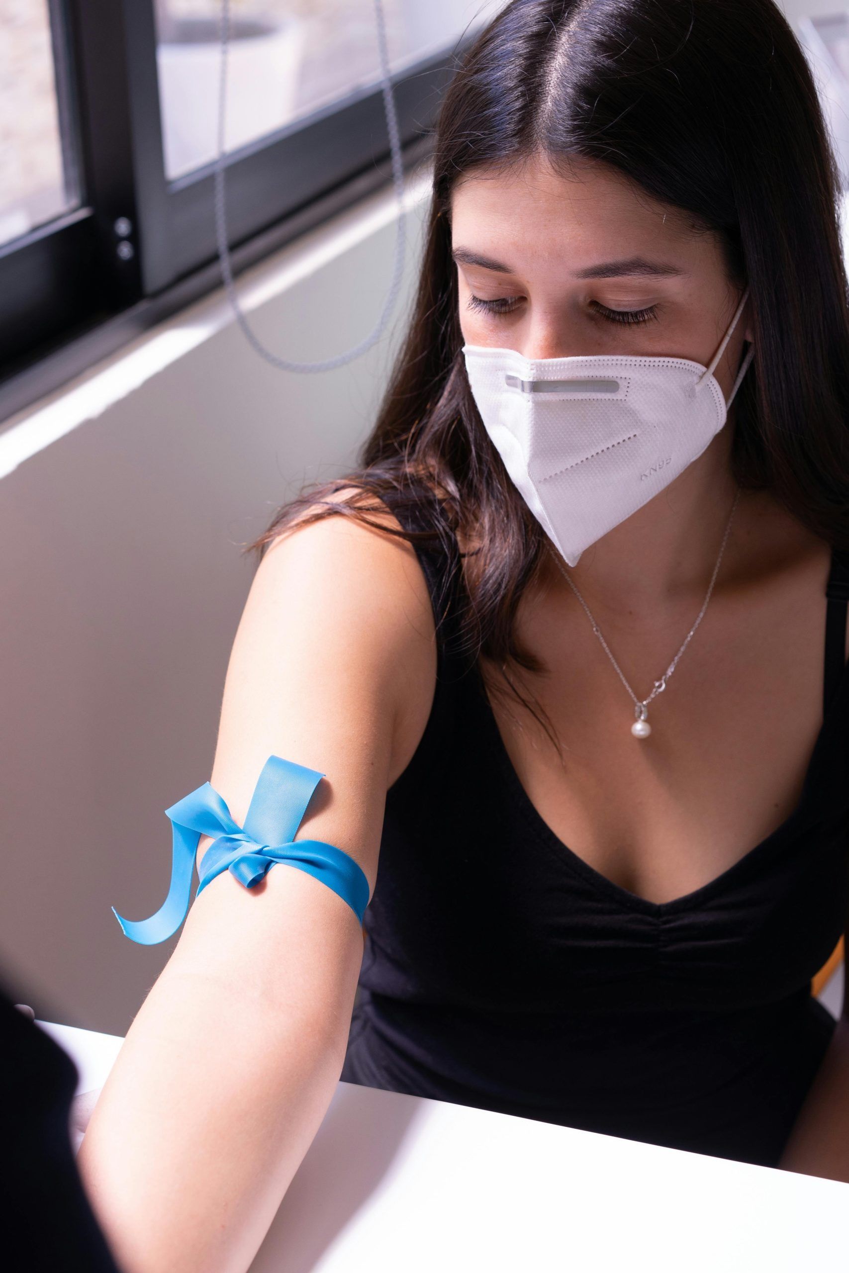 A person wearing a face mask and a blue tourniquet on their arm, preparing for a medical procedure.
