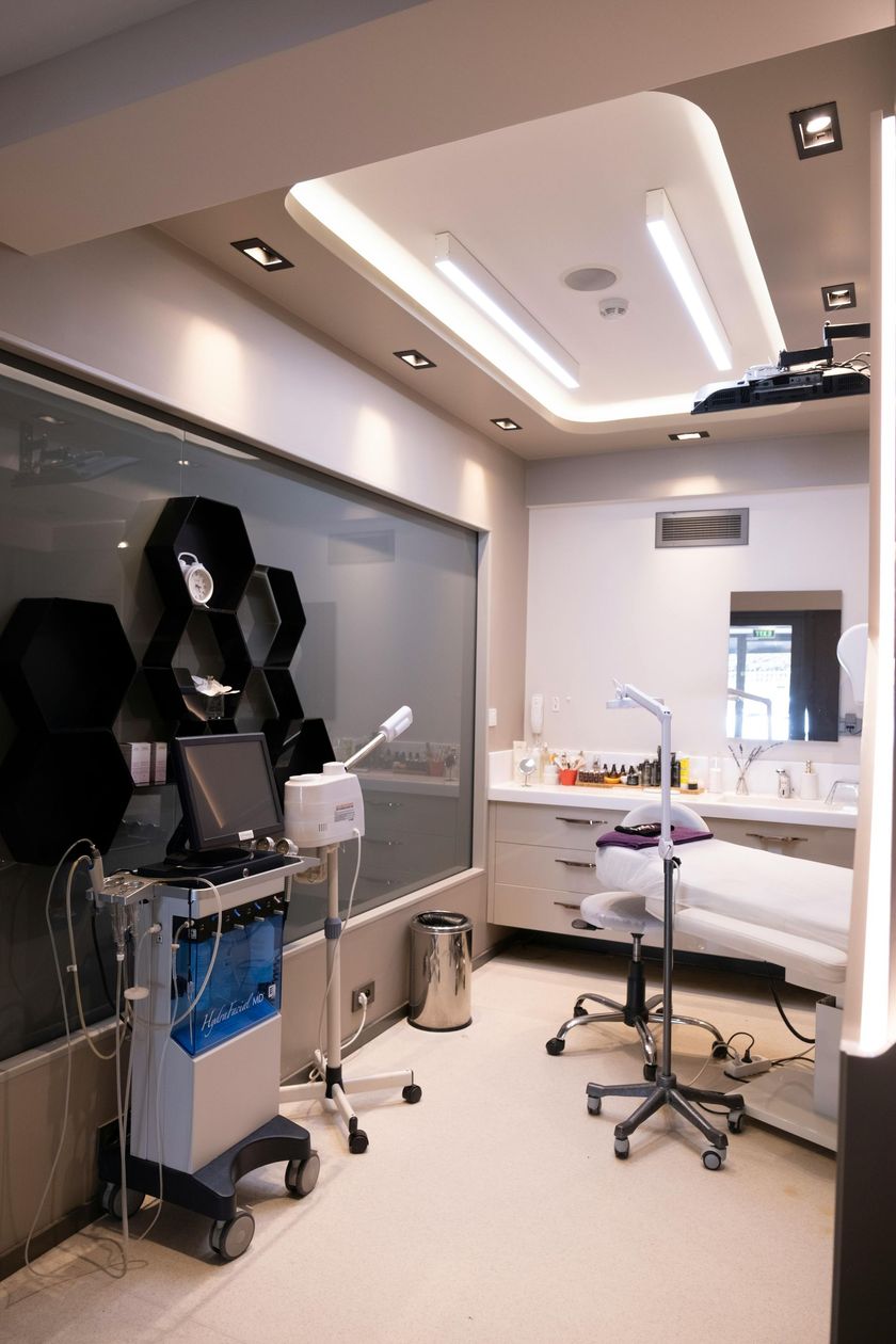 A clean, well-lit medical aesthetic treatment room featuring professional equipment, a treatment bed, and a mirror.