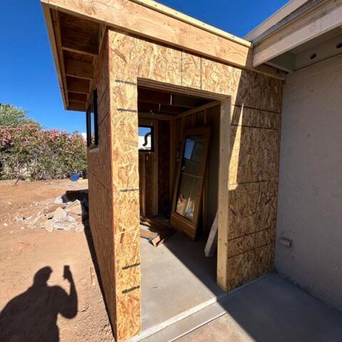 Partially built wooden entryway with open doorway and a concrete walkway in a sunny outdoor setting