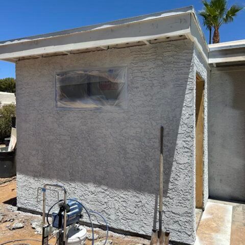 Stucco house exterior under construction with a covered window and tools in front