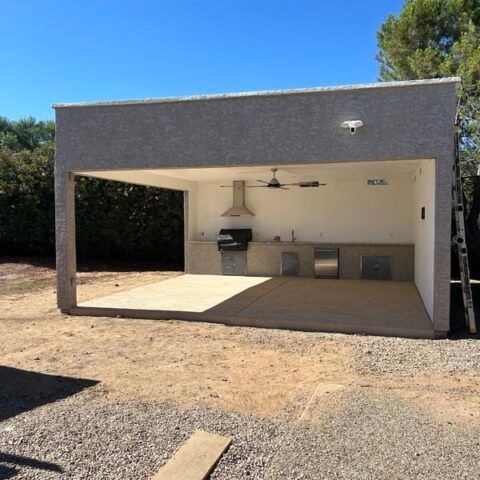 Outdoor covered patio with grill, ceiling fan, and built-in cabinets under a white stucco roof