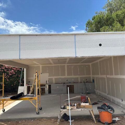 Interior of a garage under construction, with drywall, scaffolding, and tools on the floor.