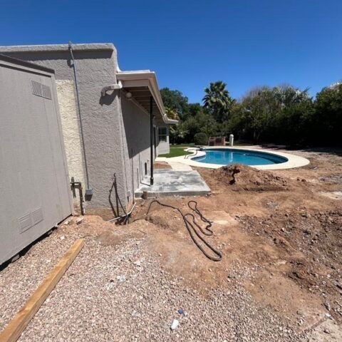 Backyard patio beside a house, with a pool and dirt yard under a clear blue sky.