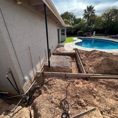 Backyard poolside construction trench beside a house, with exposed dirt and tools.