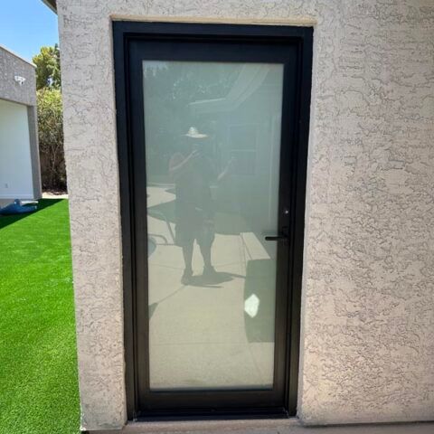 Black-framed glass door in a stucco wall beside bright green artificial grass.