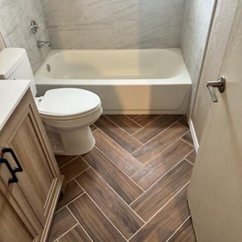 Small bathroom with a bathtub, toilet, vanity, and wood-look tile floor.