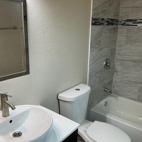 Small bathroom with sink, toilet, and bathtub with gray tile wall and mirror