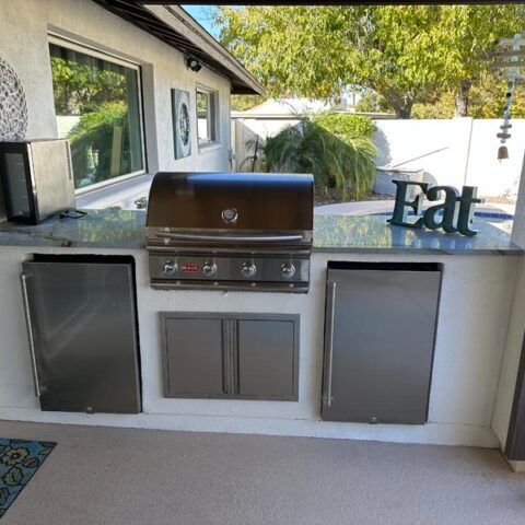 Outdoor patio with built-in grill, cabinets, and decorative “Eat” sign along a white wall.