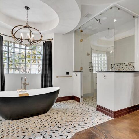 Modern bathroom with black freestanding tub, glass shower, patterned tile floor, and large window