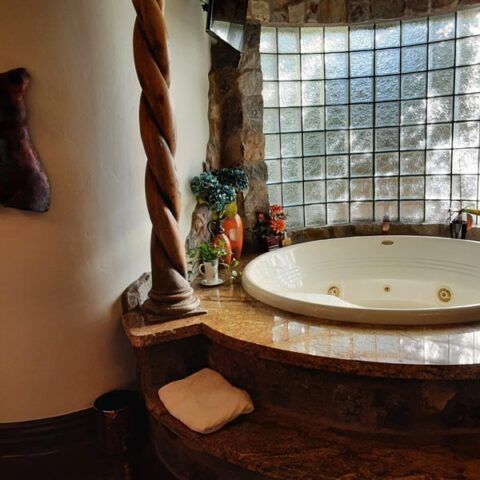 Spa bathroom with a round whirlpool tub beside a glass-block window and rustic stone accents