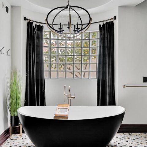 Modern bathroom with a black-and-white freestanding tub, chandelier, and window with dark curtains