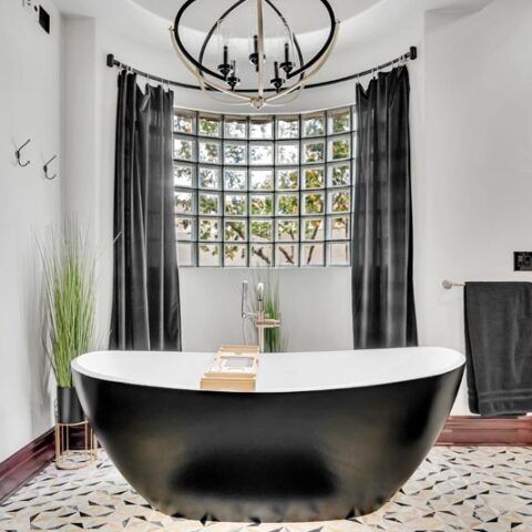 Modern bathroom with a black freestanding tub, glass-block window, and dark curtains