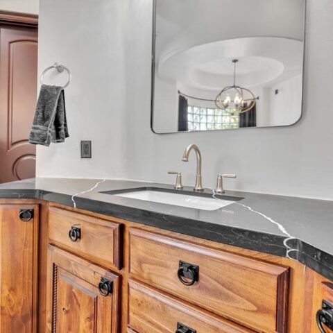 Bathroom vanity with wood cabinets, black countertop, sink, and mirrored wall