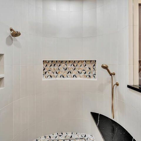 White tiled shower with brass fixtures, decorative niche, and a black shower stool or seat