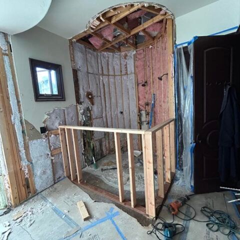 Damaged interior wall with exposed studs, broken doorway, and temporary wood railing during renovation