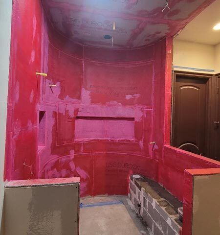 Partially renovated bathroom with bright pink walls, exposed wall framing, and a dark wooden door.