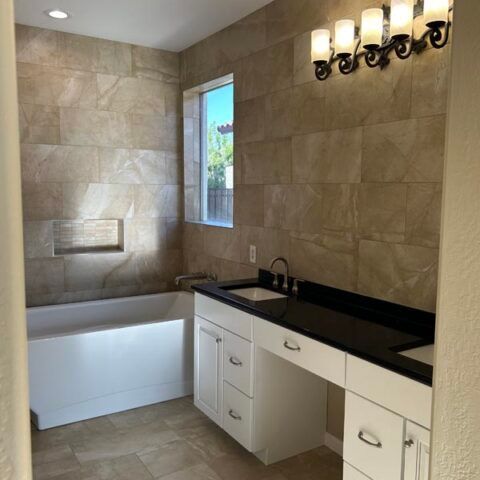 Modern bathroom with white tub, black vanity countertop, beige tile walls, and wall sconces