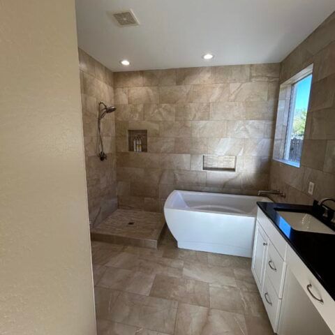 Modern beige-tiled bathroom with walk-in shower, freestanding tub, and vanity with black countertop