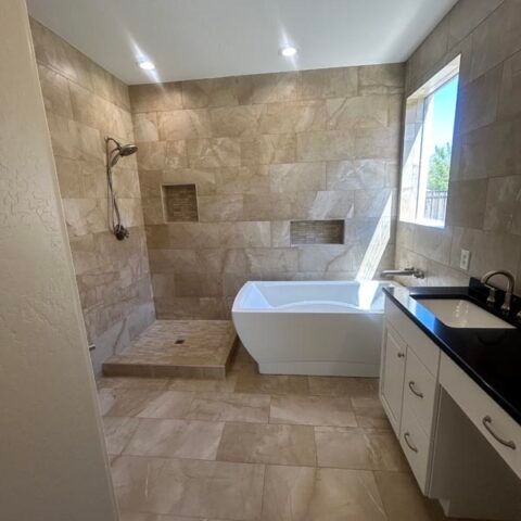 Modern beige-tile bathroom with walk-in shower, soaking tub, and vanity by a window.
