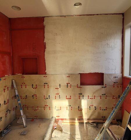 Partially renovated room with exposed red walls, tiled half-wall, and a ladder on each side