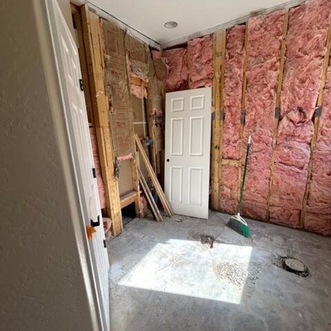 Unfinished room with pink insulation exposed, white door, and construction materials on the floor.