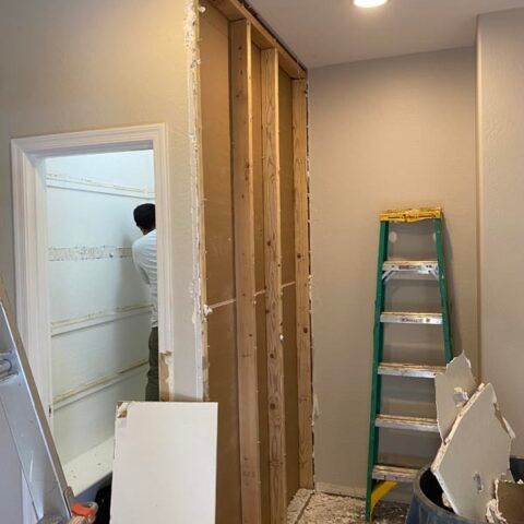 Partially renovated room with exposed wall studs, a green ladder, and construction debris near a doorway